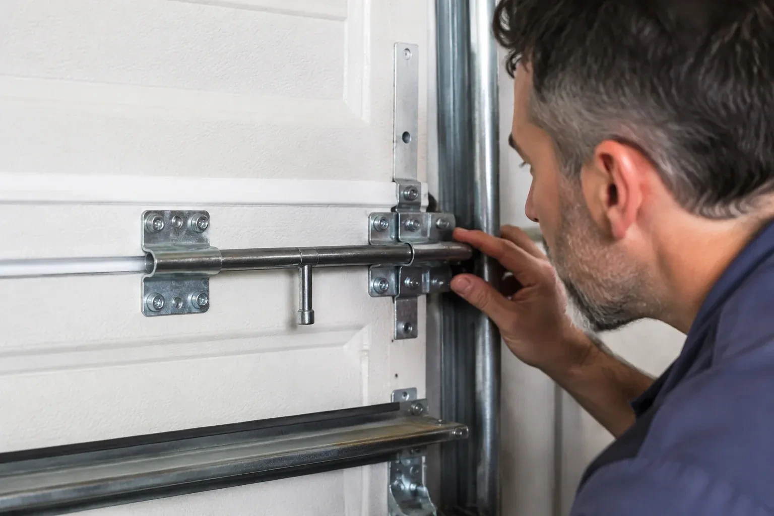 Person leaning close to a white paneled door, one hand on a metal slide-bolt bar mounted across the panel. — Garage Door Manual Lock Repair, London