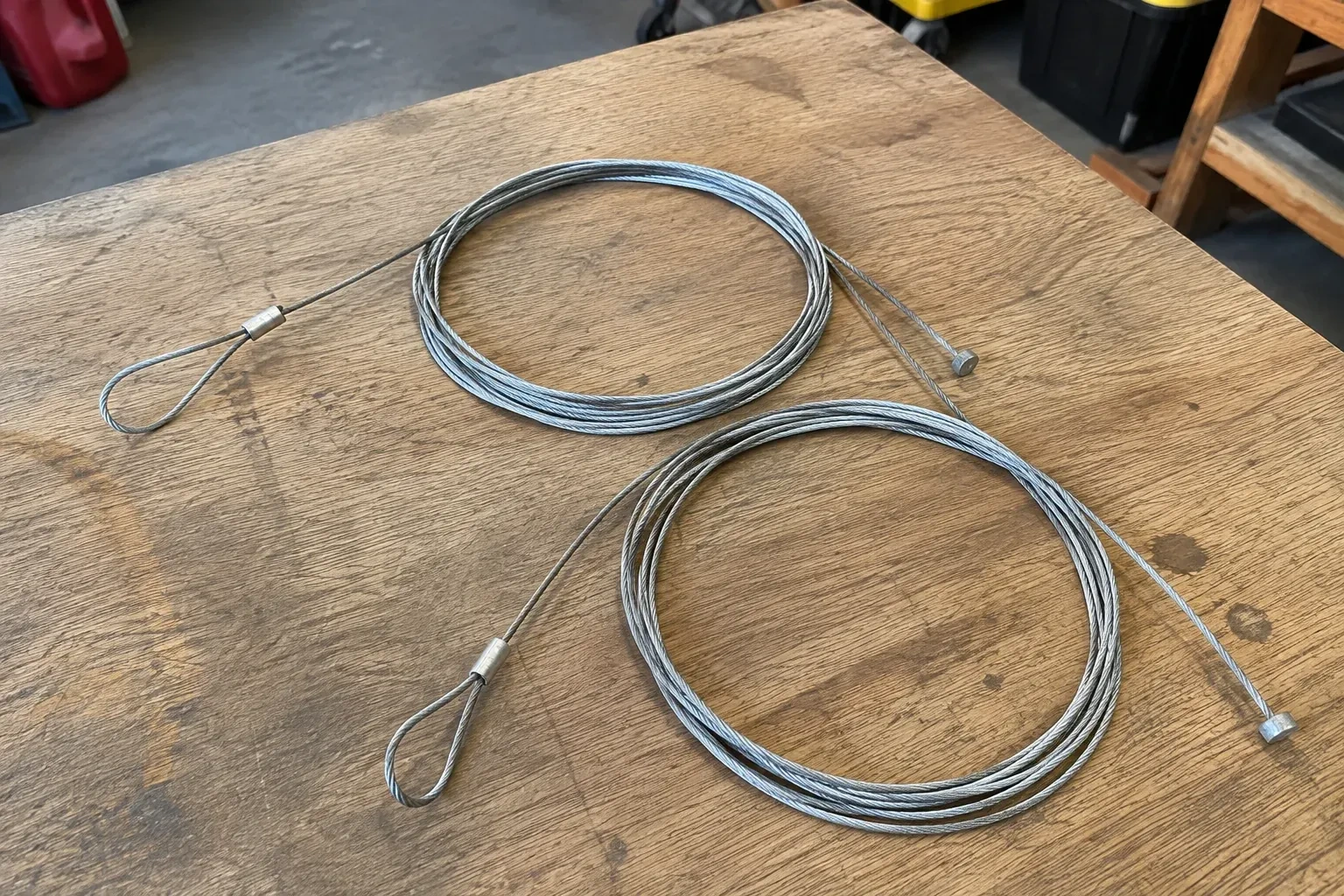 Two coiled steel cables with loop and stop ends on a workbench. — Garage Door Cable Replacement, London